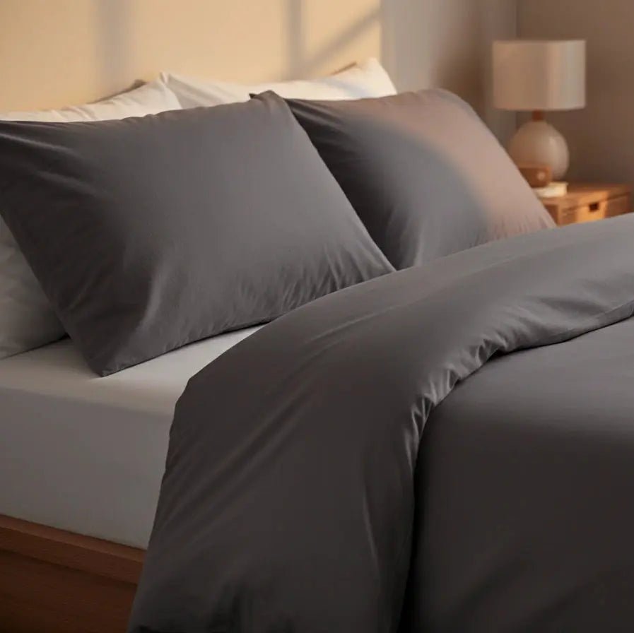 Detailfoto antraciet dekbedovertrek tweepersoons met bijpassende kussenslopen op modern bed, warme sfeerverlichting.