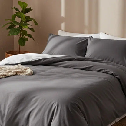 Luxe antraciet dekbedovertrek 240x220 lits-jumeaux van hotelkwaliteit katoen, opgemaakt met witte onderlaag en gebreide beige plaid in een warme, minimalistische slaapkamer met groene kamerplant.