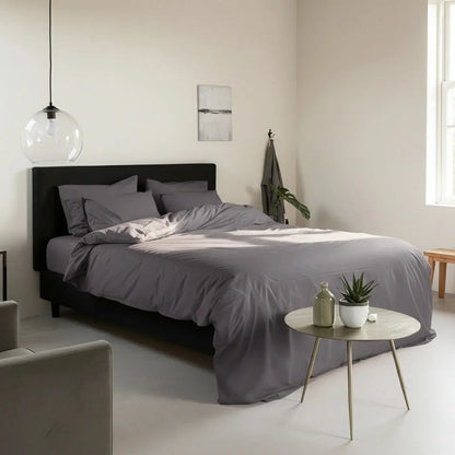Antraciet dekbedovertrek 240x220 lits-jumeaux in een minimalistische Scandinavische slaapkamer met zwart boxspringbed, zachte natuurlijk lichtinval, houten bijzettafel met plant en modern interieur in rustige aardetinten.