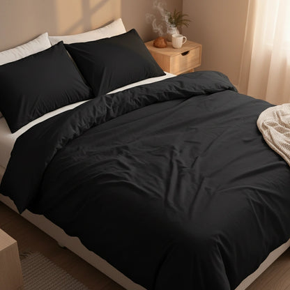 Zwart dekbedovertrek 240x220 lits-jumeaux in luxe hotelstijl slaapkamer, gemaakt van zachte hotelkwaliteit stof. Stijlvol effen zwart beddengoed op een strak opgemaakt bed met twee zwarte kussens en beige nachtmeubel, warme sfeerverlichting en rustige minimalistische uitstraling.